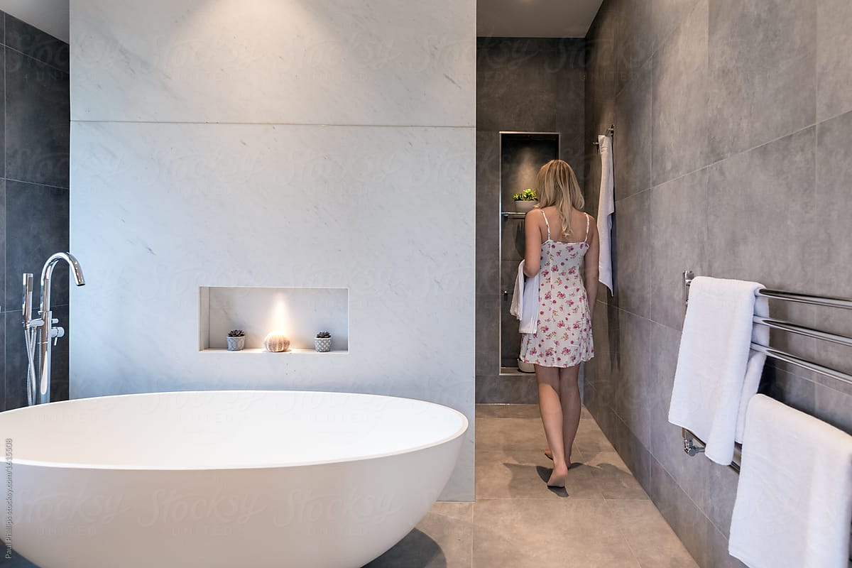 Modern bathroom with oval white freestanding bath. Woman walking to the shower behind.