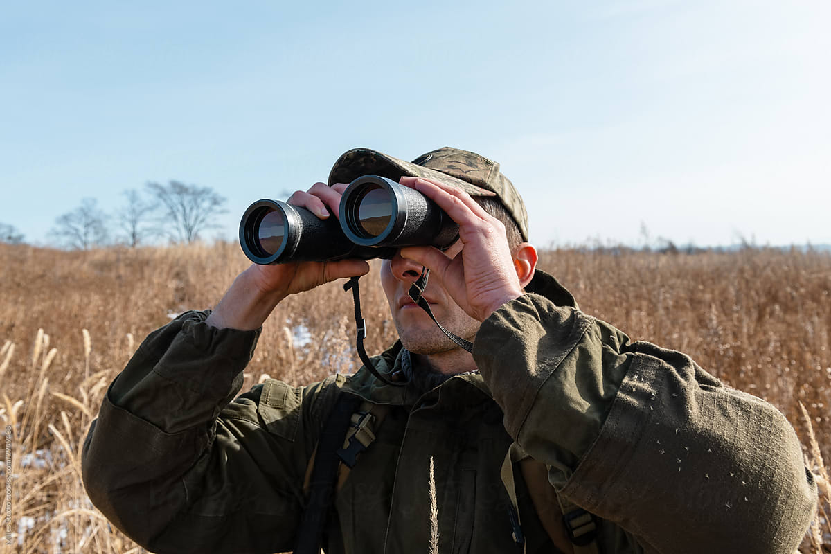 Man in camouflage using binoculars in nature