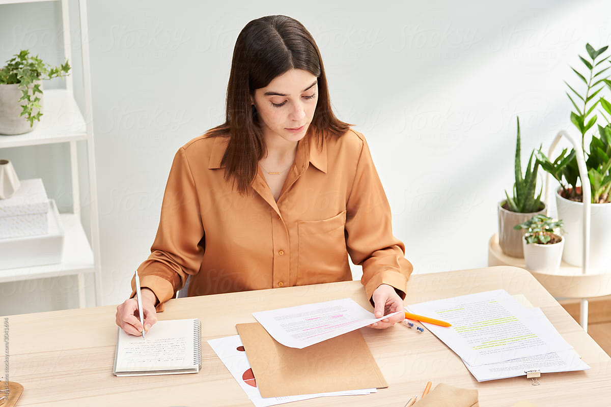 Young female freelancer analyzing papers in home office