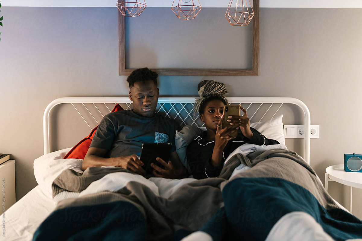 African American couple with gadgets resting in bed