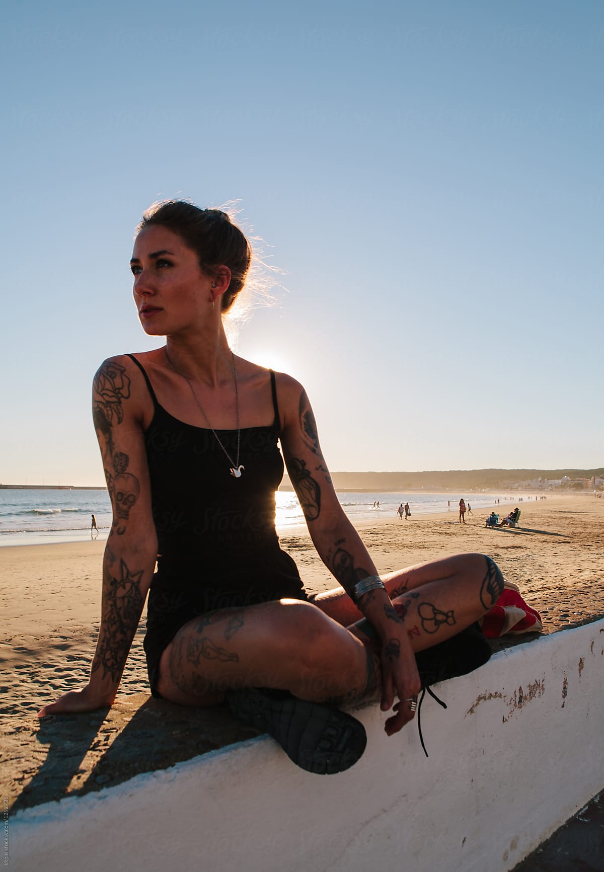 Beautiful woman sitting on a wall next to a beach with the sun behind