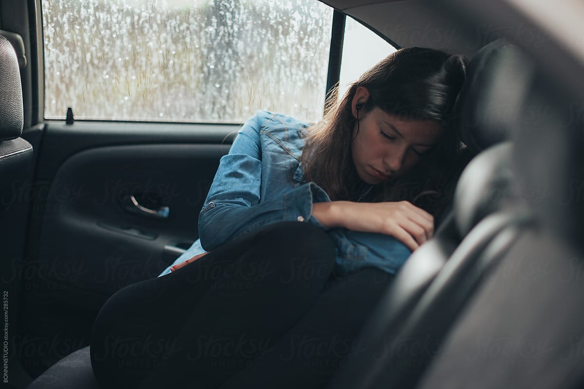 Tired young woman sleeping and listening music  inside a car. Road trip.