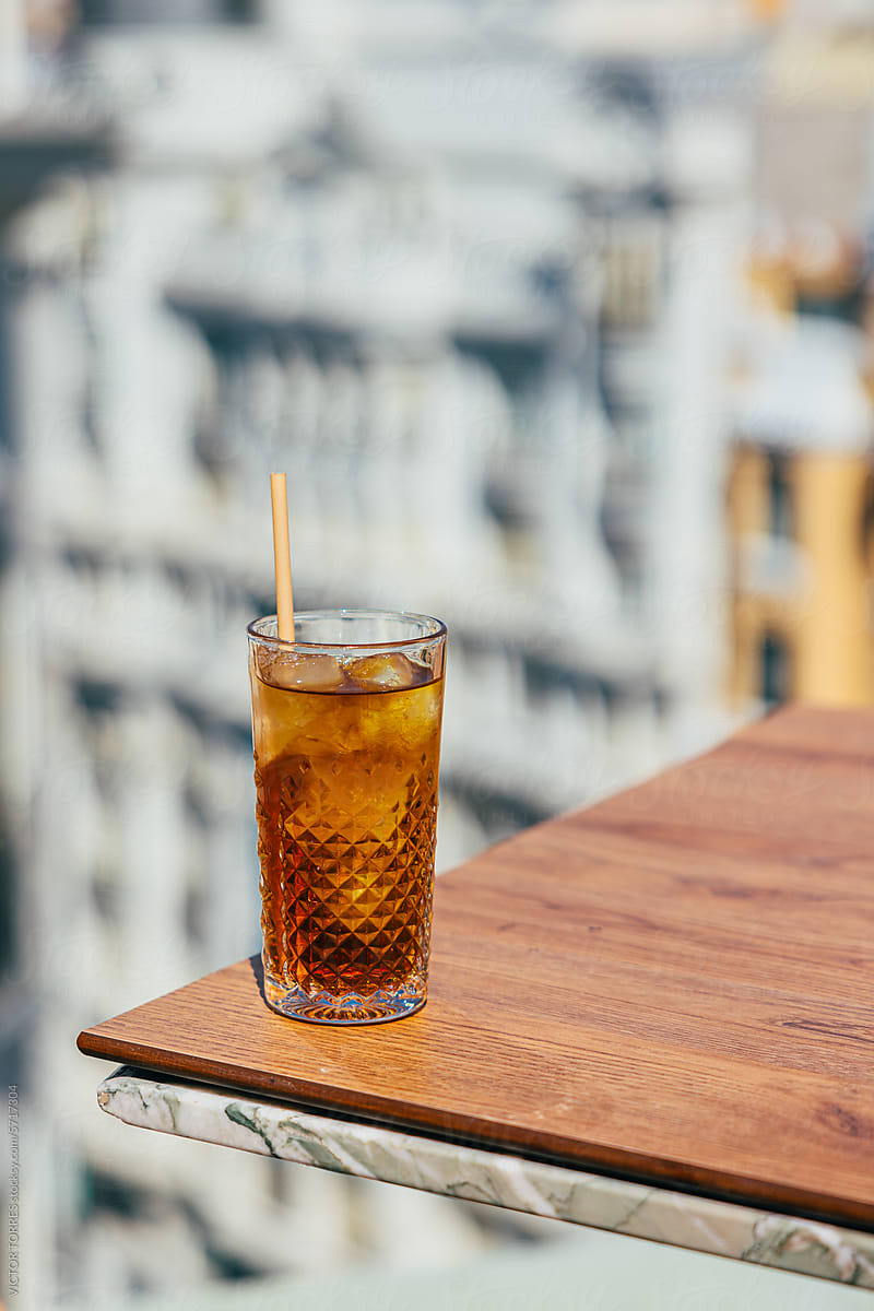Single cold drink with a straw, resting on a wooden edge