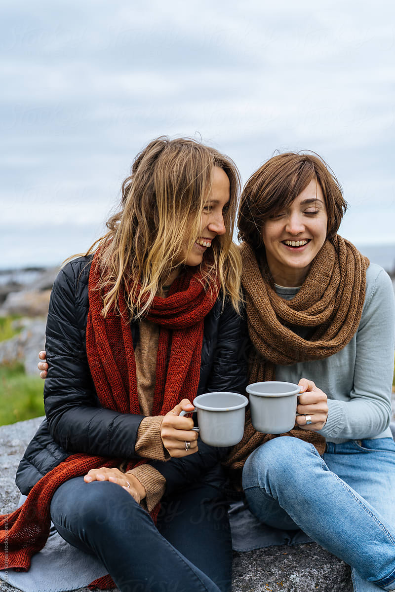 Two women clanging cups of tea outside