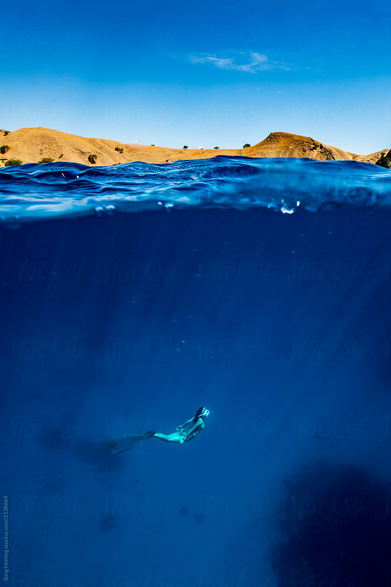 Free diver half underwater with mountains
