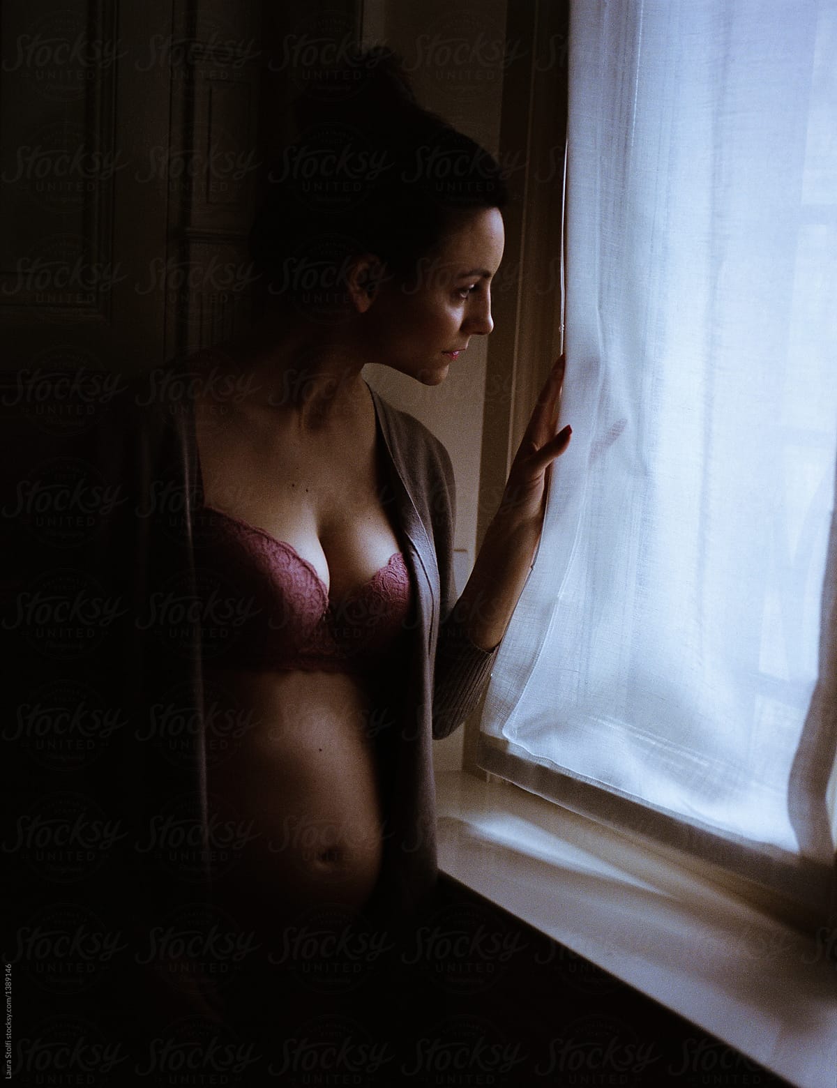 Film portrait of pregnant woman peering out of window