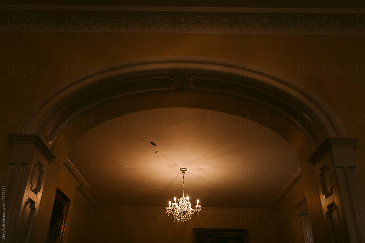 Burning ornamental chandelier on ceiling in aged country estate