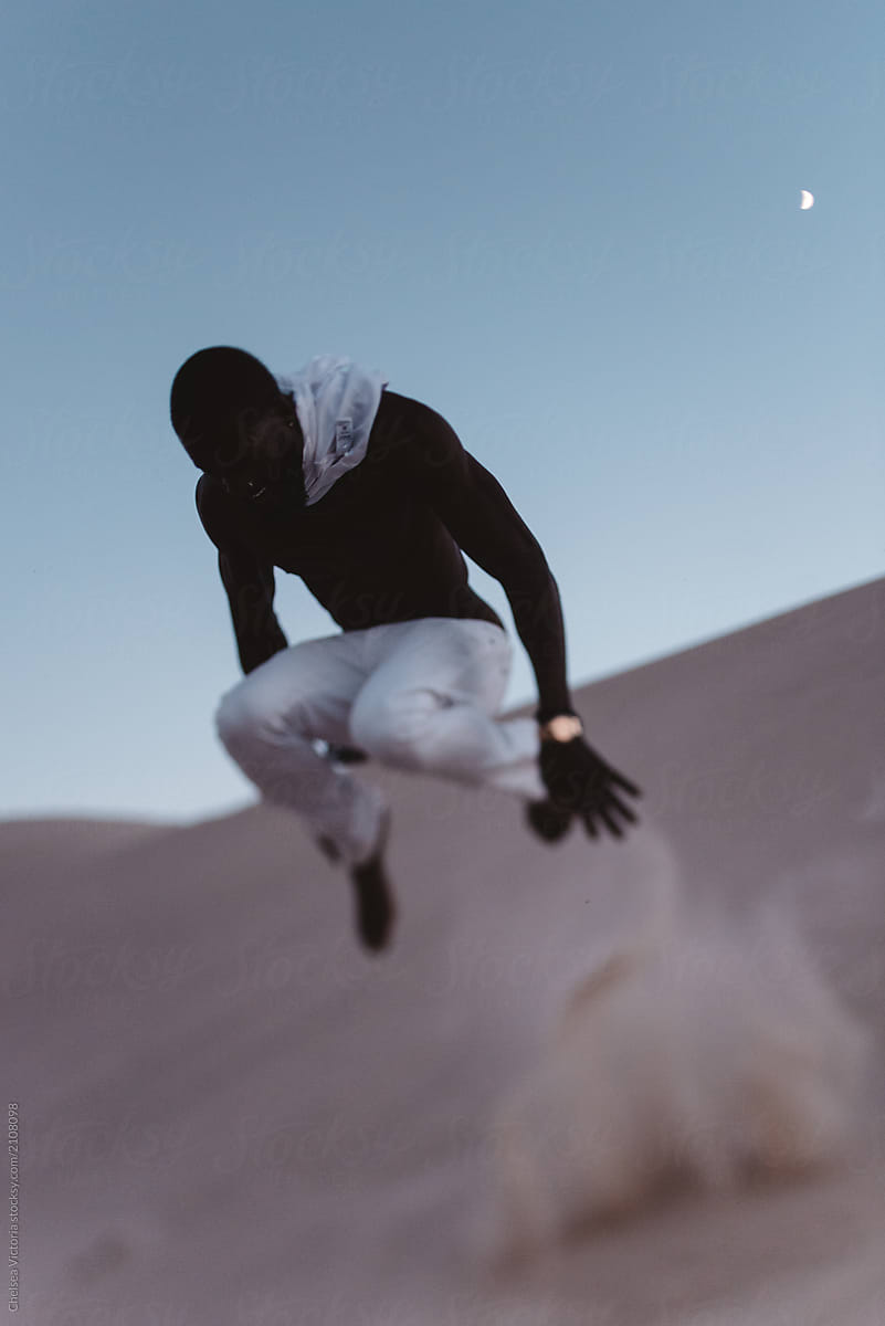 A young black man jumping in dunes of sand at night