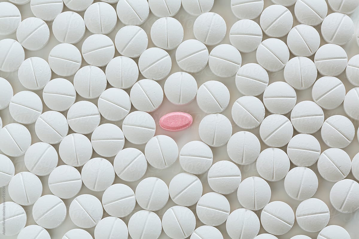 One pink pill surrounded by white prescription pills on white background