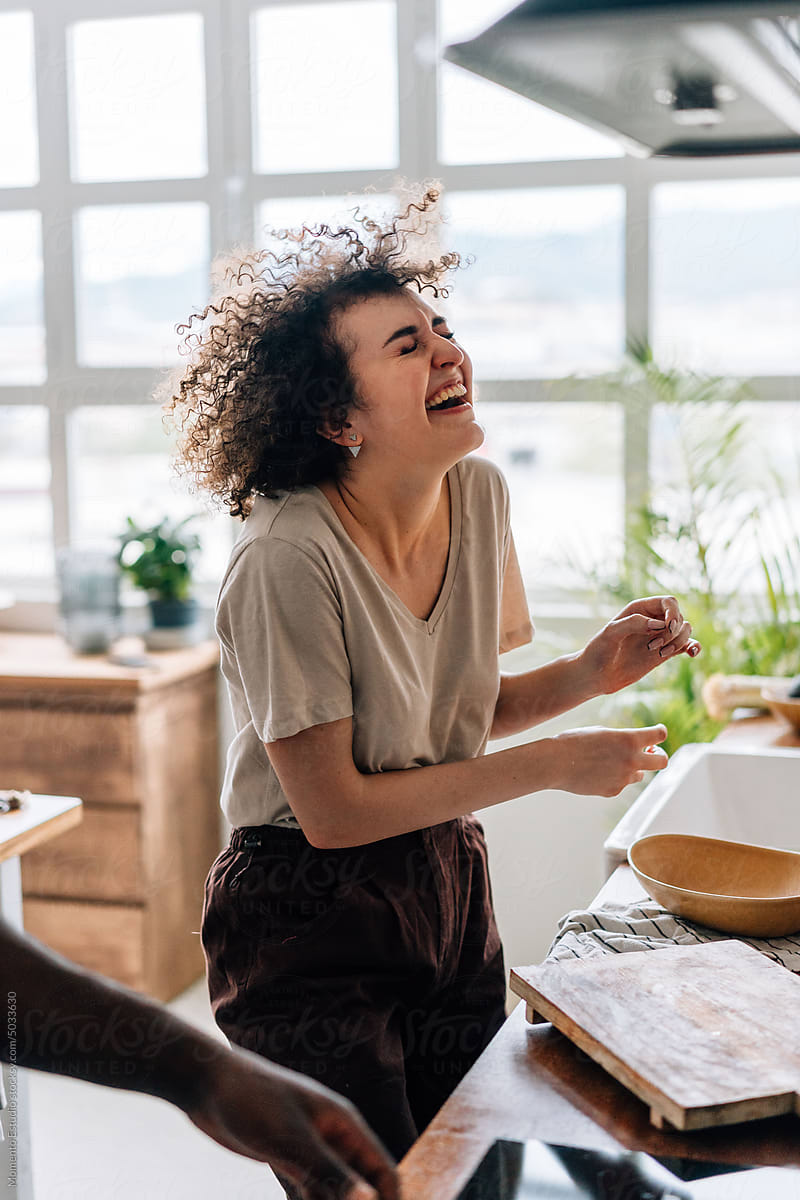 Cheerful woman bursting into laughter while cooking with friends