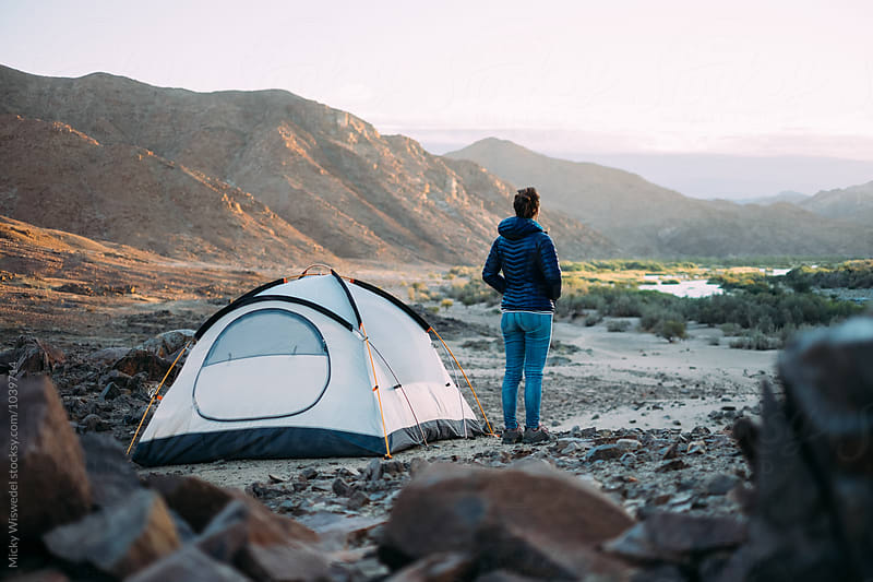 Hiker standing outside her tent in a rugged scenic desert landscape