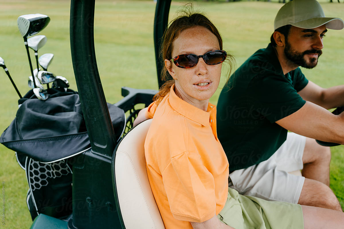 A man and a woman drive a golf car on the course