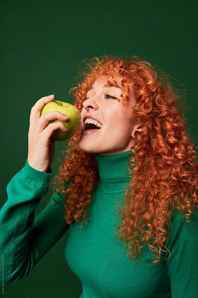 Cheerful ginger woman eating apple