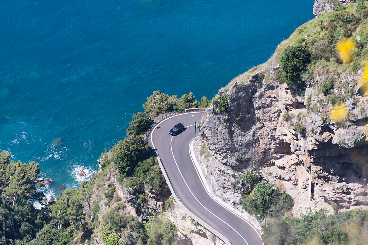 A winding road on cliff next to the ocean with a car coming around the corner