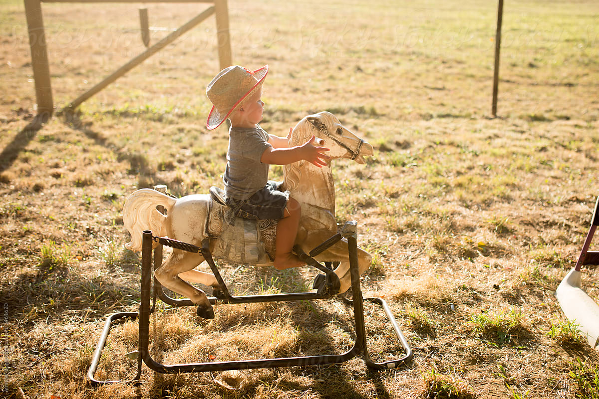 Cute toddler in cowboy hat rides rocking horse on springs