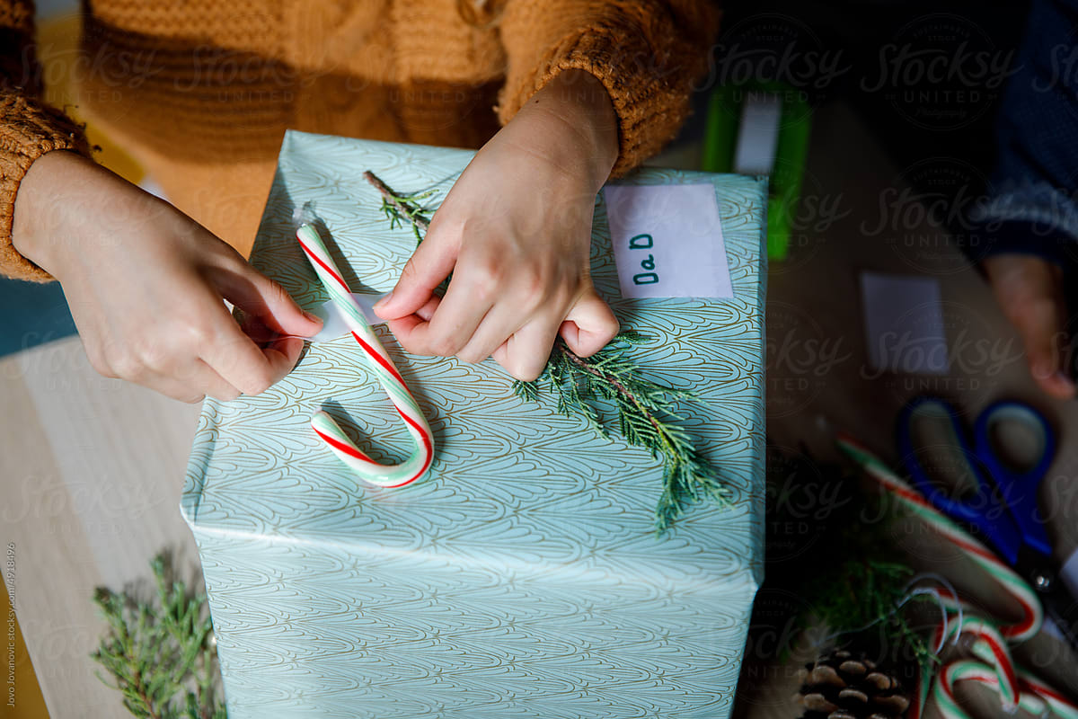 Girl decorating Christmas gift with candy cane and spruce for dad