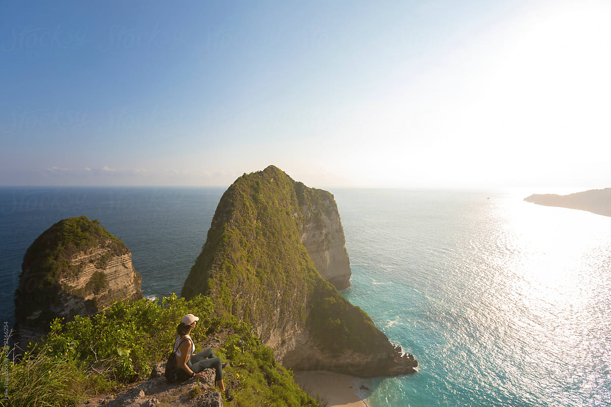 Young asian woman is sitting on a rock in Nusa Penida overlooking the ocean towards Bali