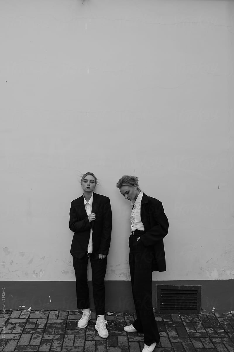 black and white photo of two sisters in black formal suits against a white wall while walking around the city
