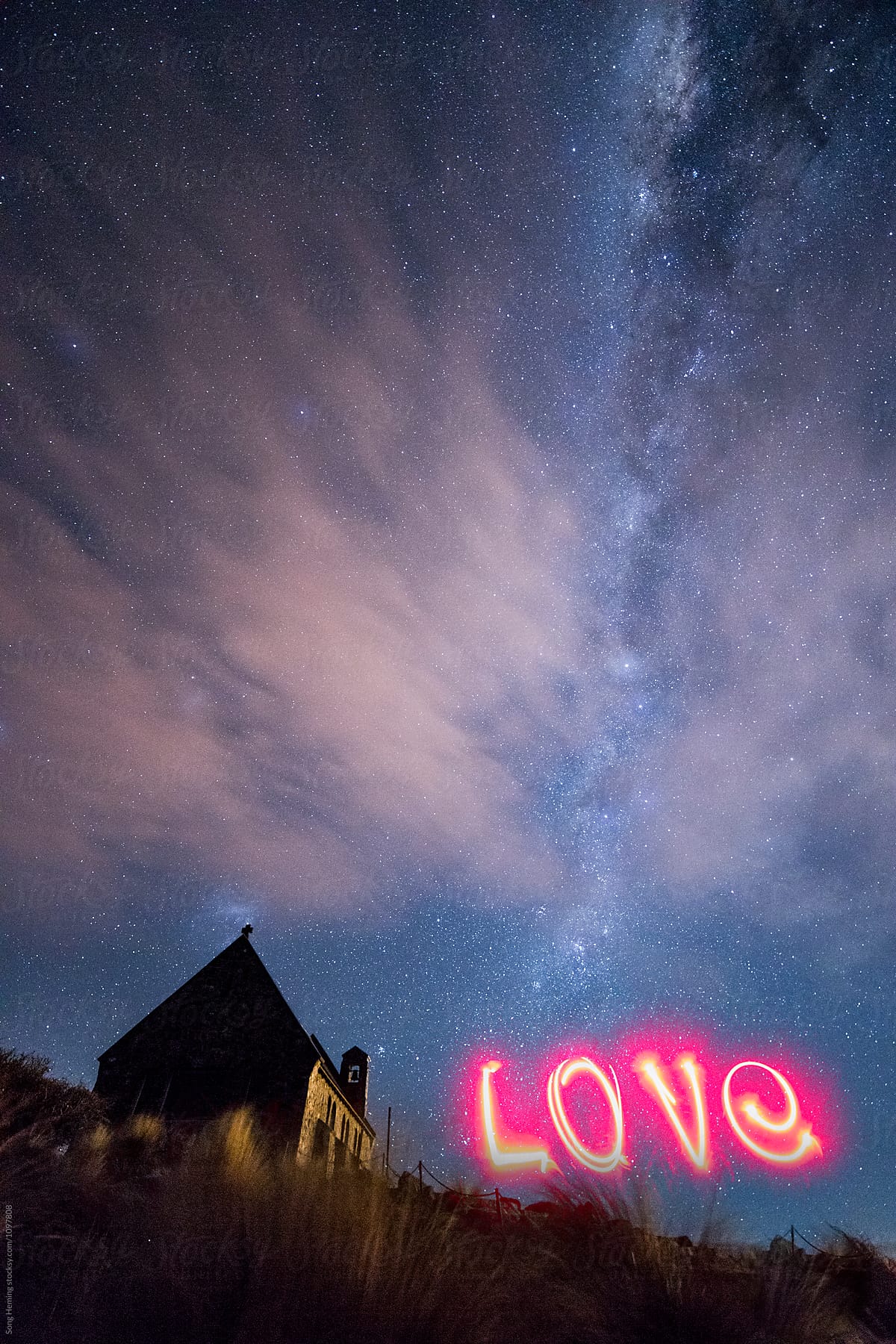 A woman writing the word 'love' with red light under the Galaxy,