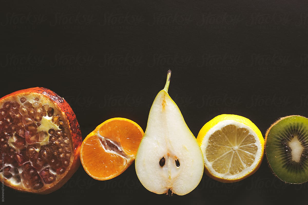 Overhead of sliced variety of fruits on black background.