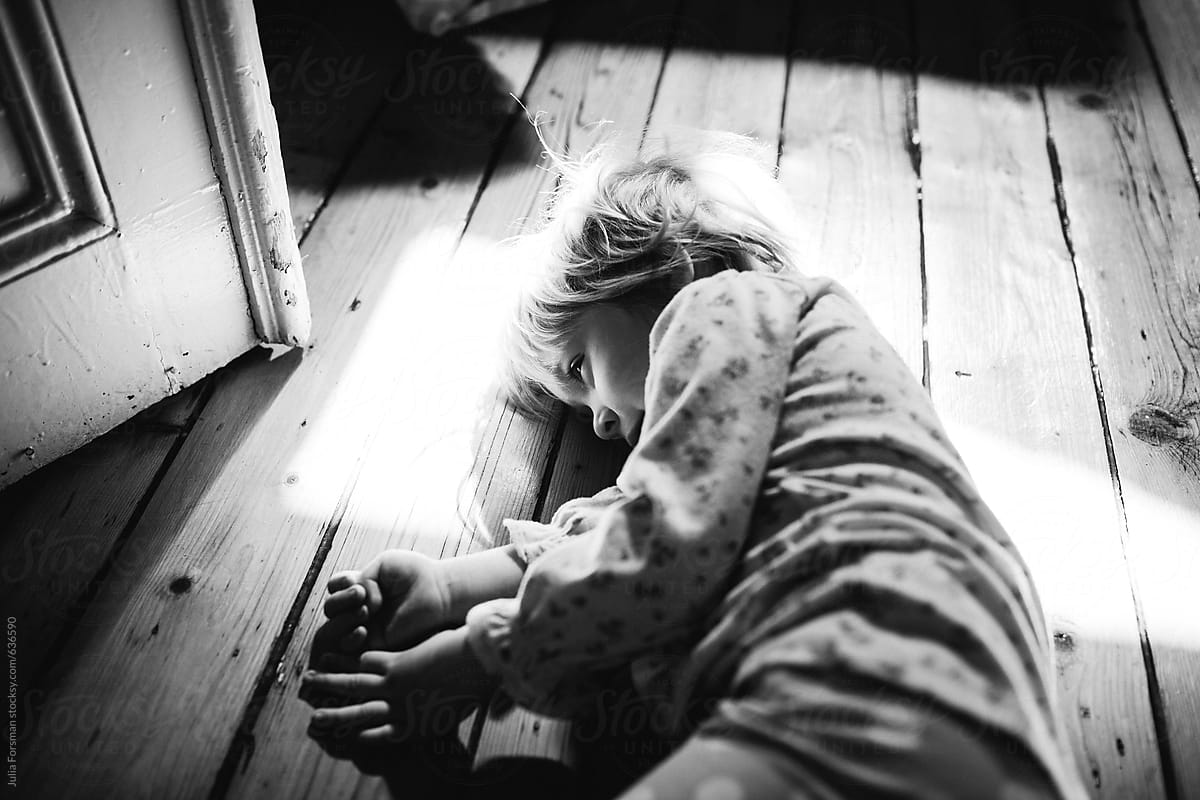 Little girl lying an a wooden floor in a patch of light.