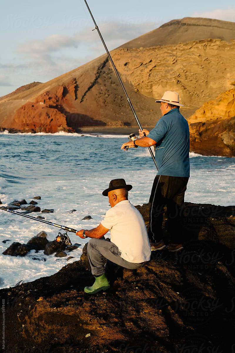Two local fishermen engage in fishing atop a cliff by the seashore