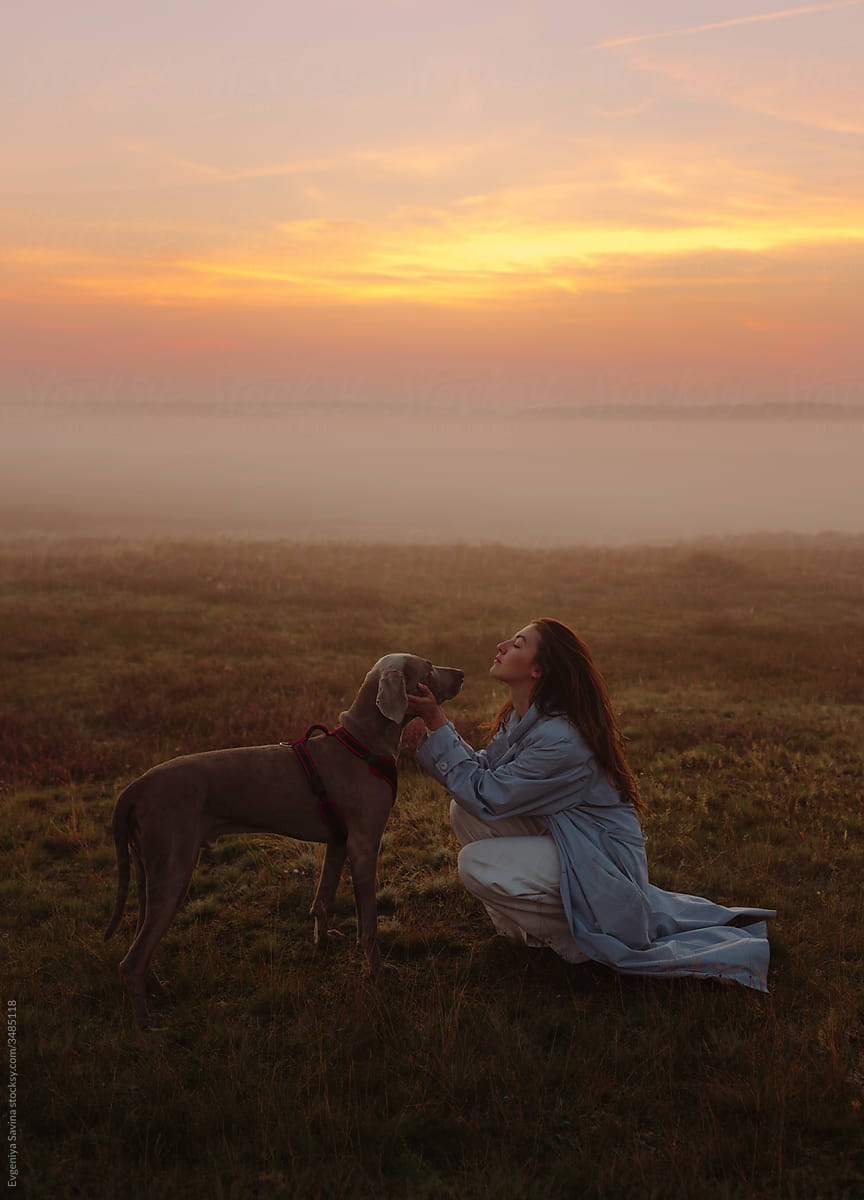 A girl in a blue coat with a dog in the foggy field