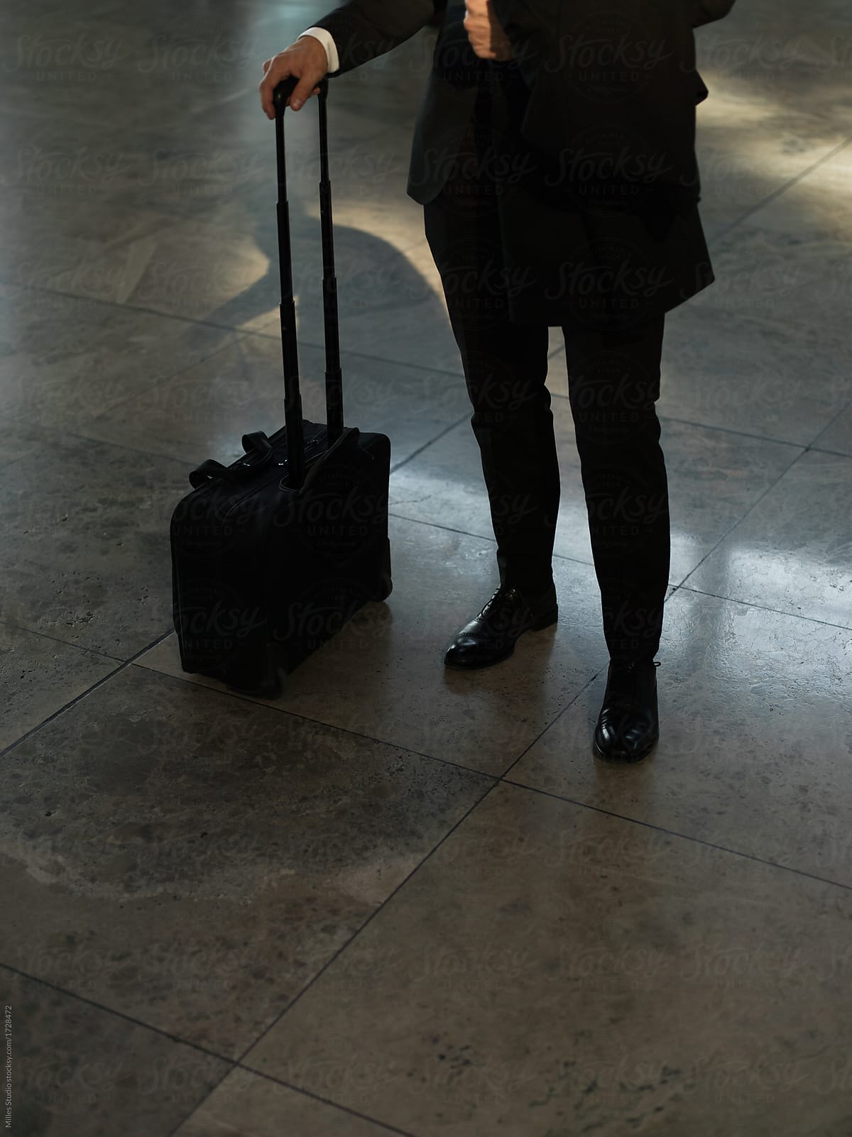Crop man in black standing with suitcase