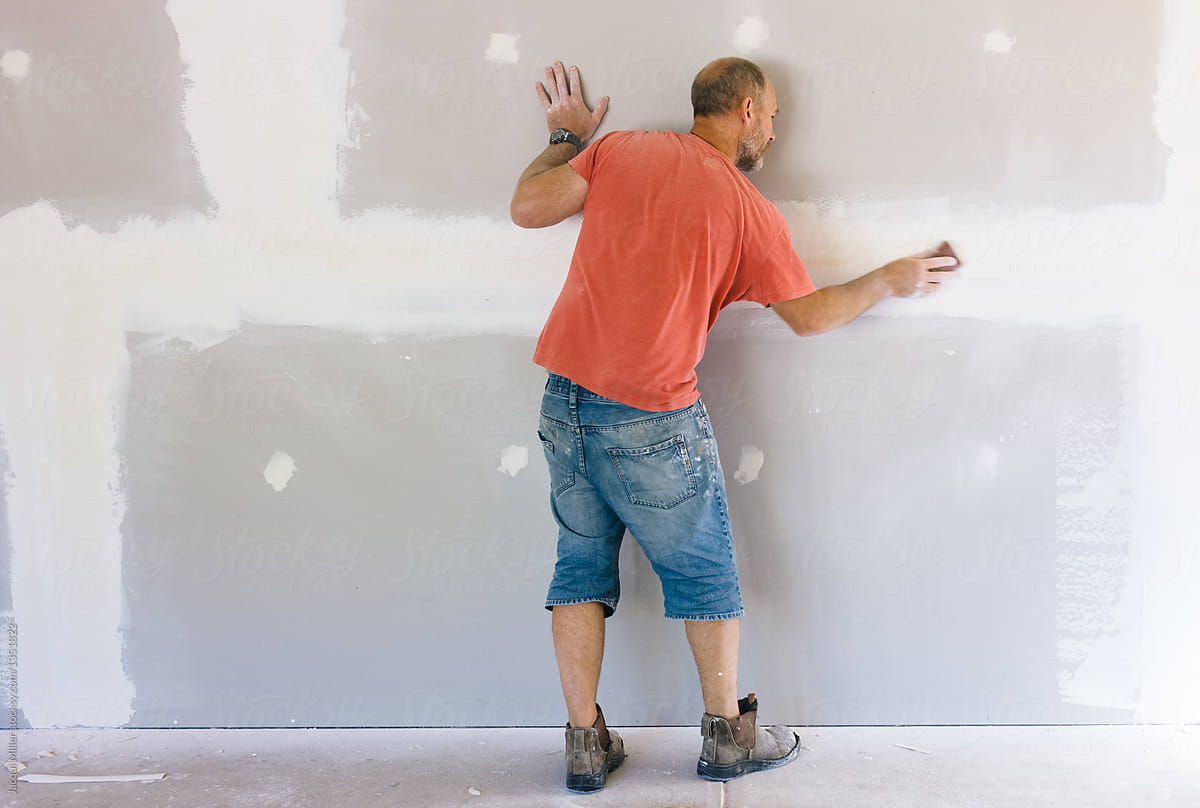 Home handyman sanding plasterboard wall - horizontal