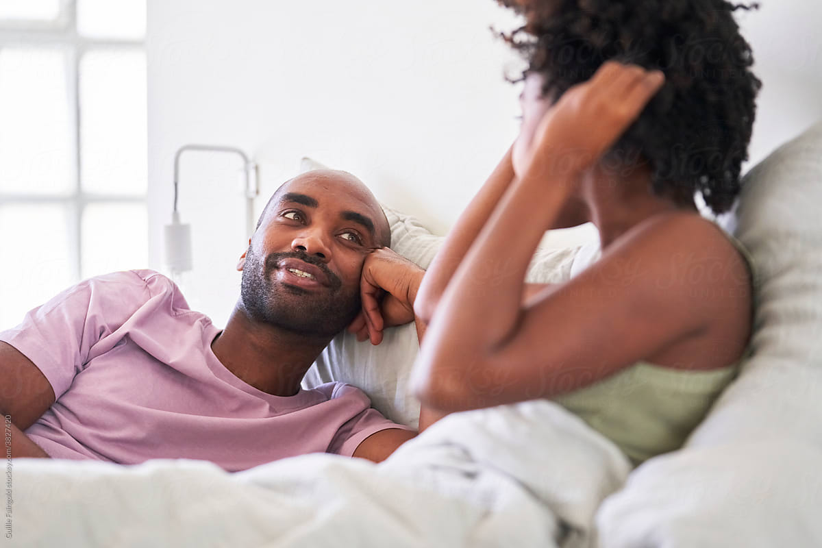 Black couple telling in bed in white light interior.