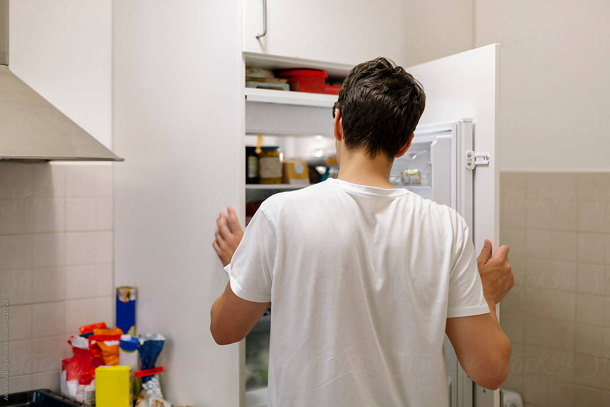 Man stands and looks inside of an open fridge.