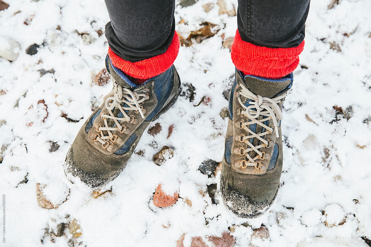 POV shot of Woman’s feet with hiking boots and red socks in the snow