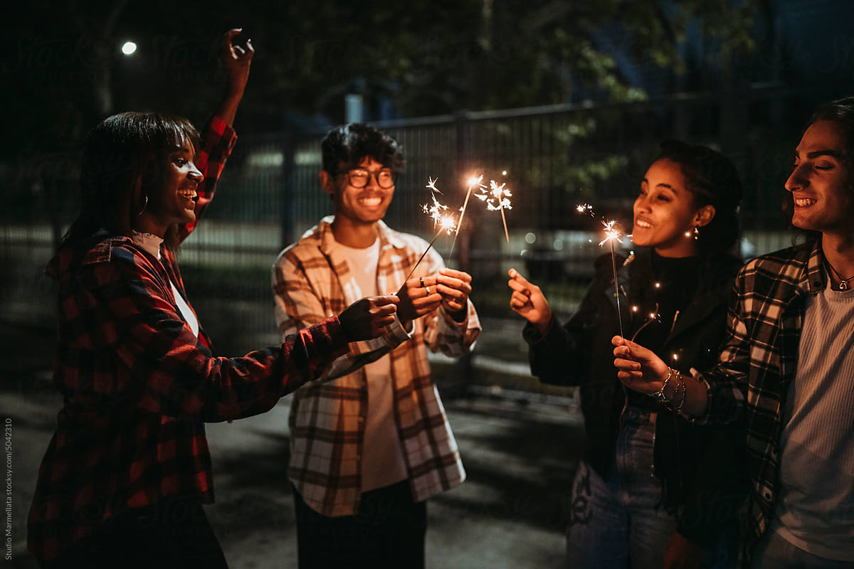 Happy diverse friends with burning sparklers on street