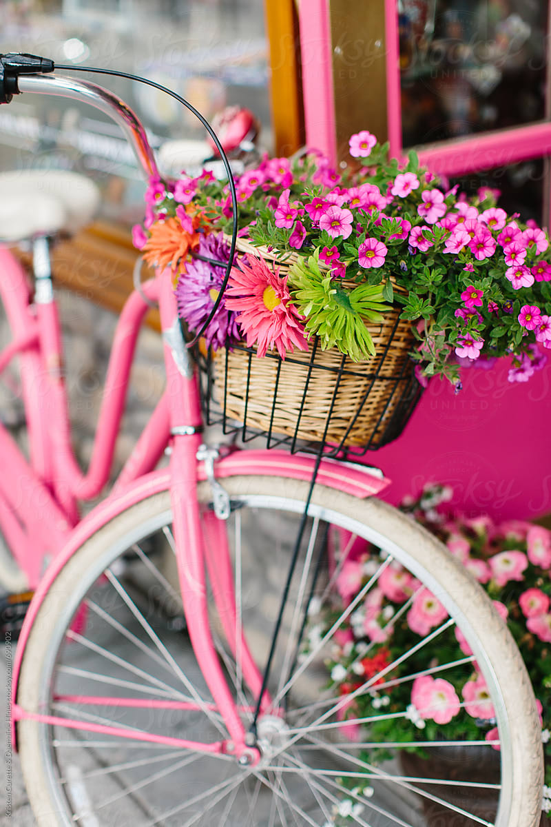 A pink cruiser bike with a basket full of assorted flowers