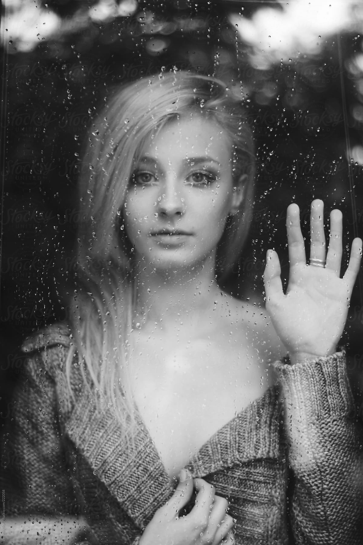 Beautiful young woman  standing at the window watching the rain