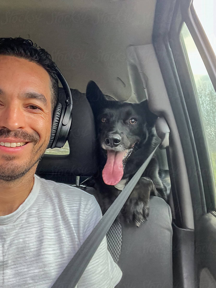 Selfie of a man smiling with seat belt next to his black dog