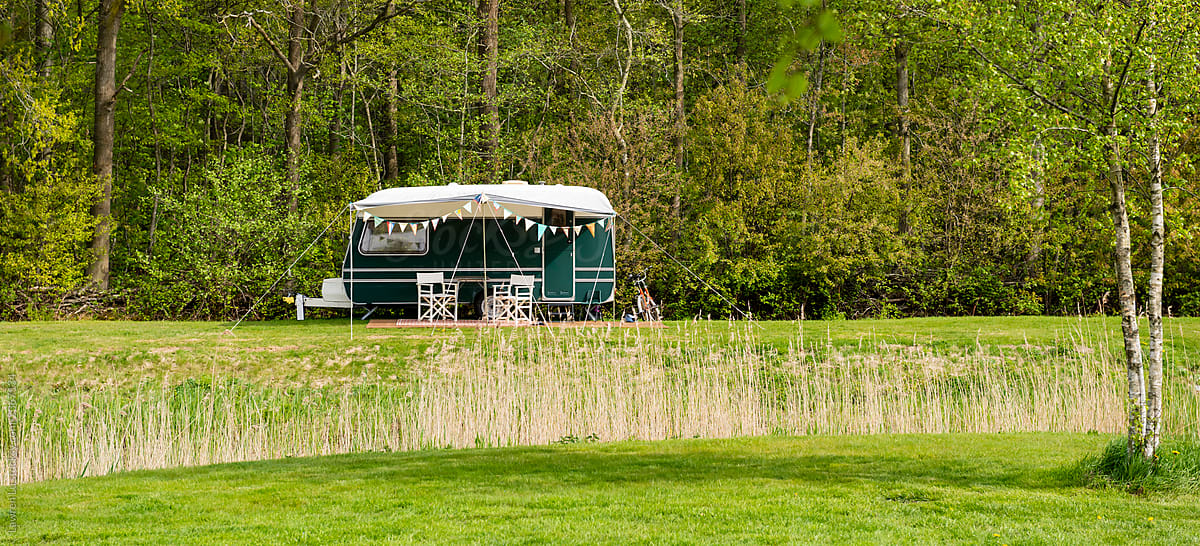 Caravan trailer on green lawn against forest in sunny spring