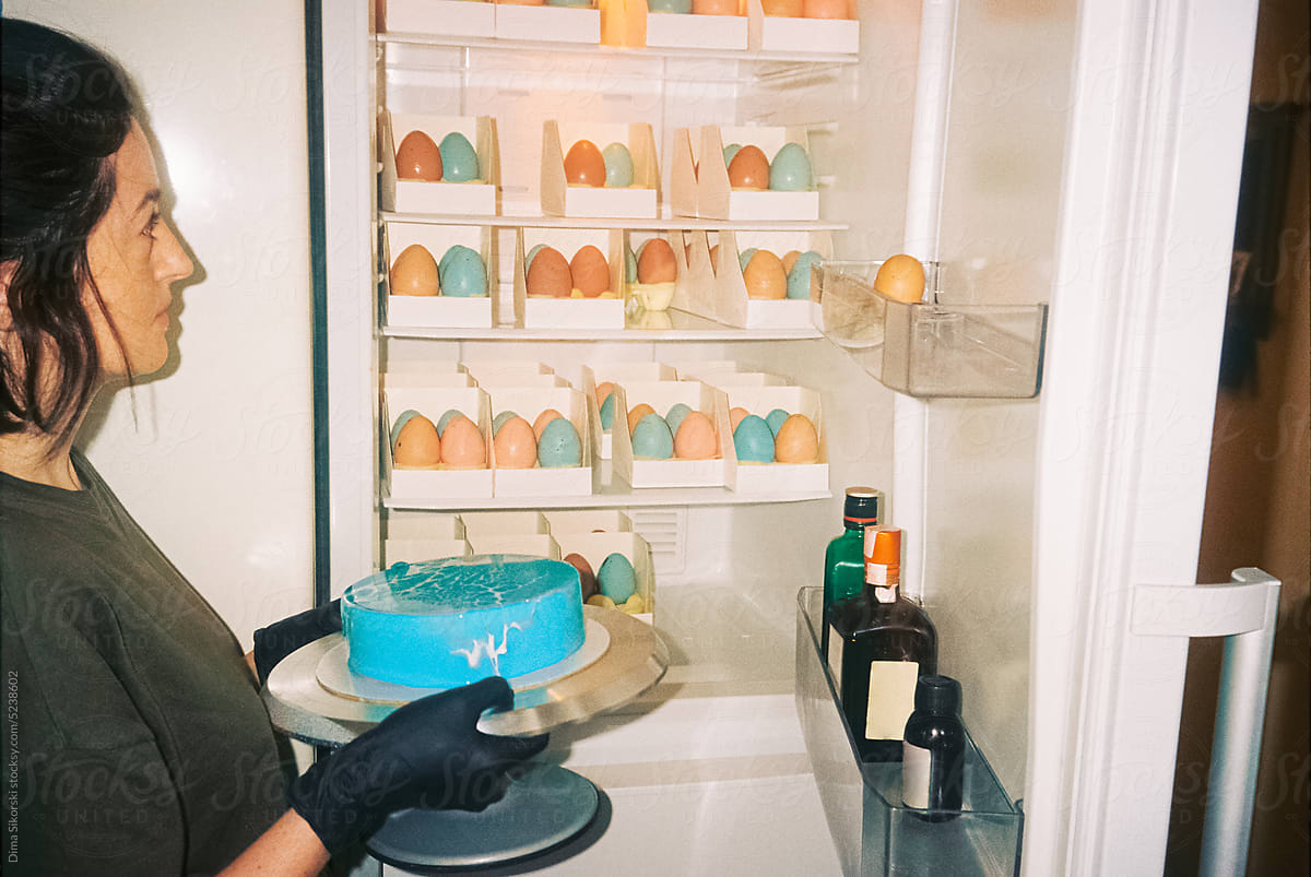 A girl with a cake near the fridge filled with Easter eggs