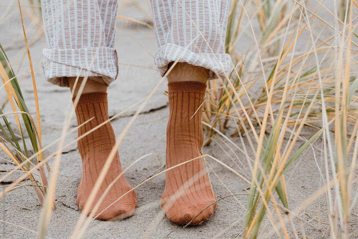 Two feet standing on a beach with sand and grass.
