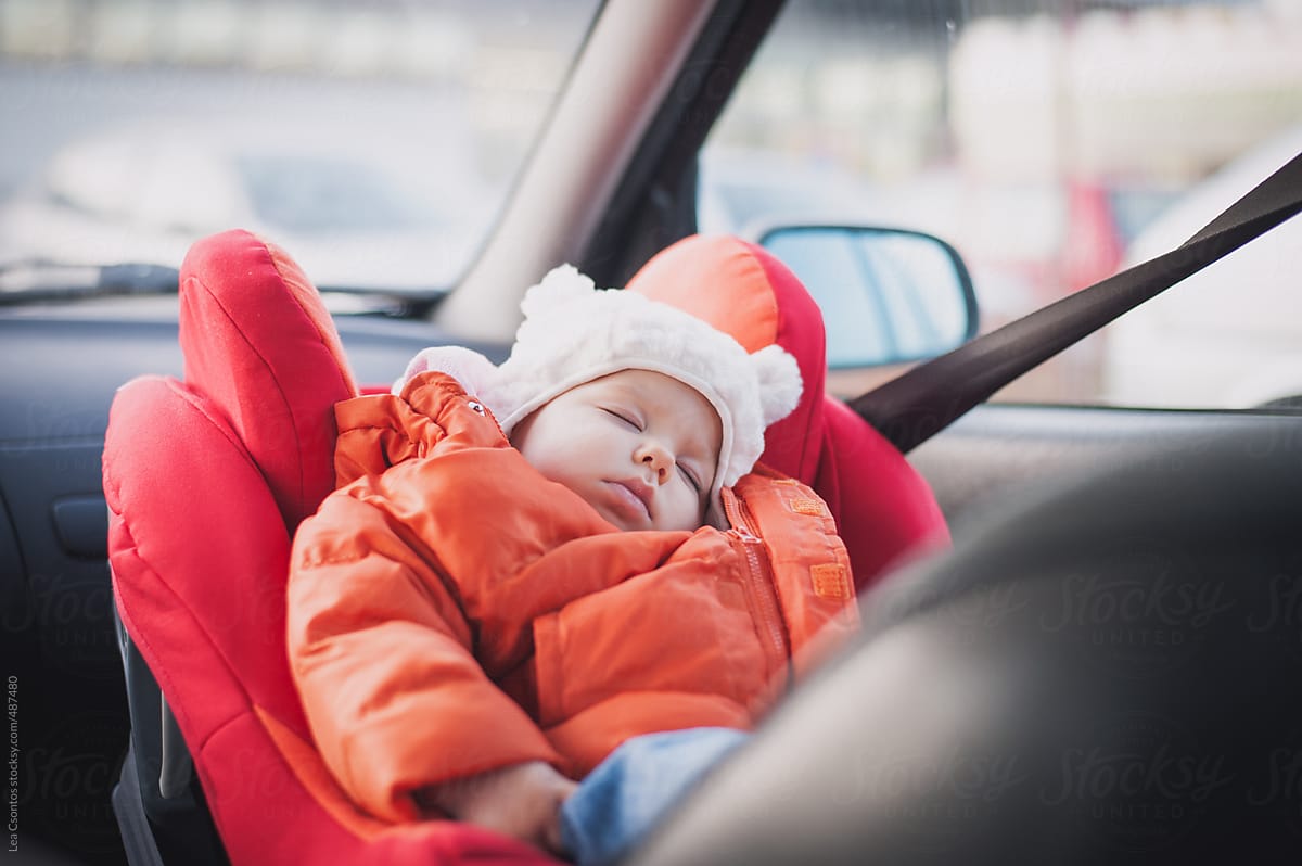 Baby sleeping peacefully in a car seat wearing a jacket and furry hat