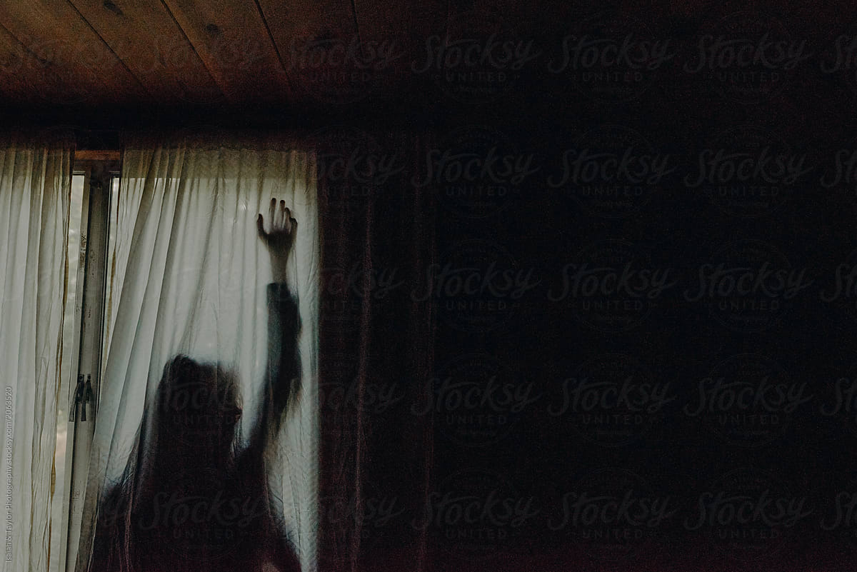 A shadowed silhouette of a person hiding behind a curtain reaching hand out against surface