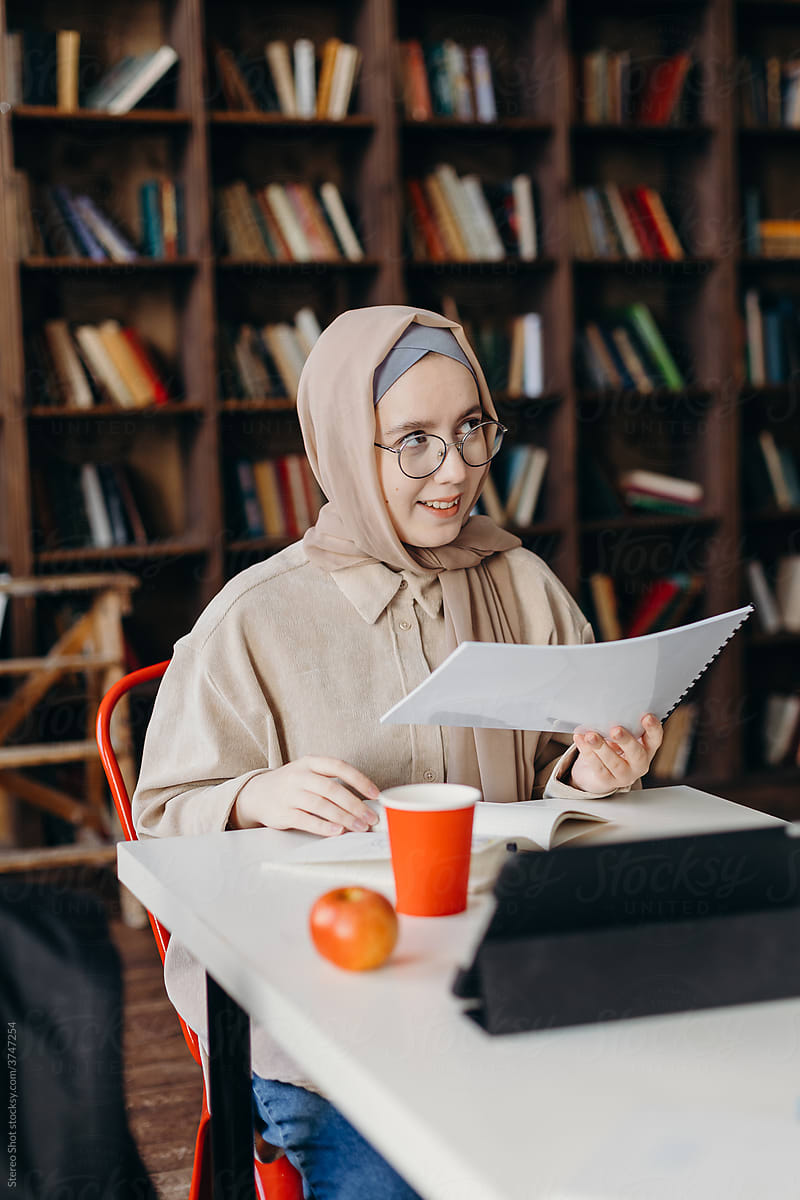 Cheerful Muslim female student reading assignment in library