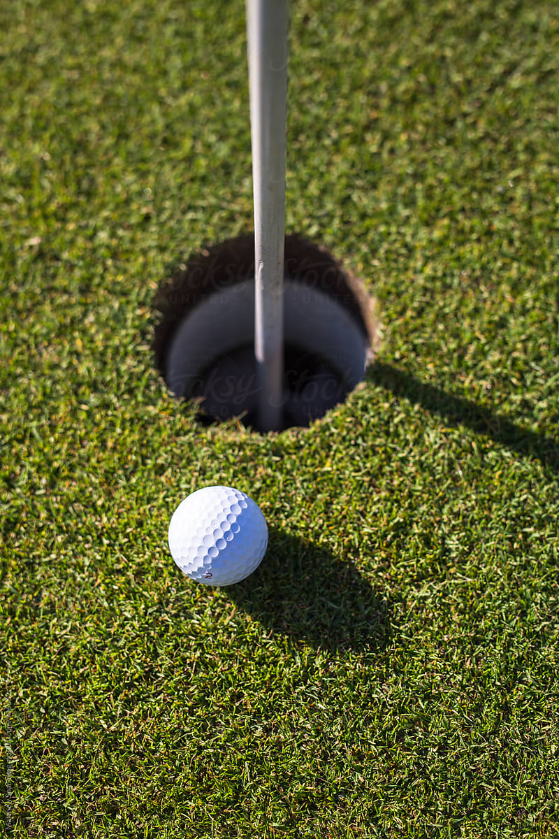 Golf ball near hole on putting green, vertical