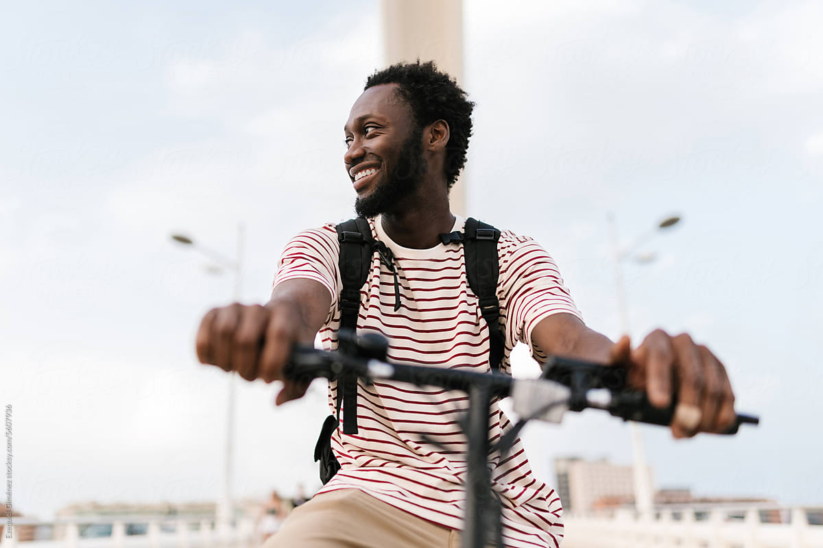 Cheerful black man riding electric bike in city