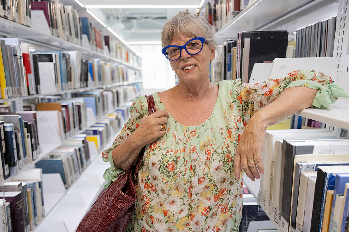 Portrait smiling senior woman leaning on library bookshelf.