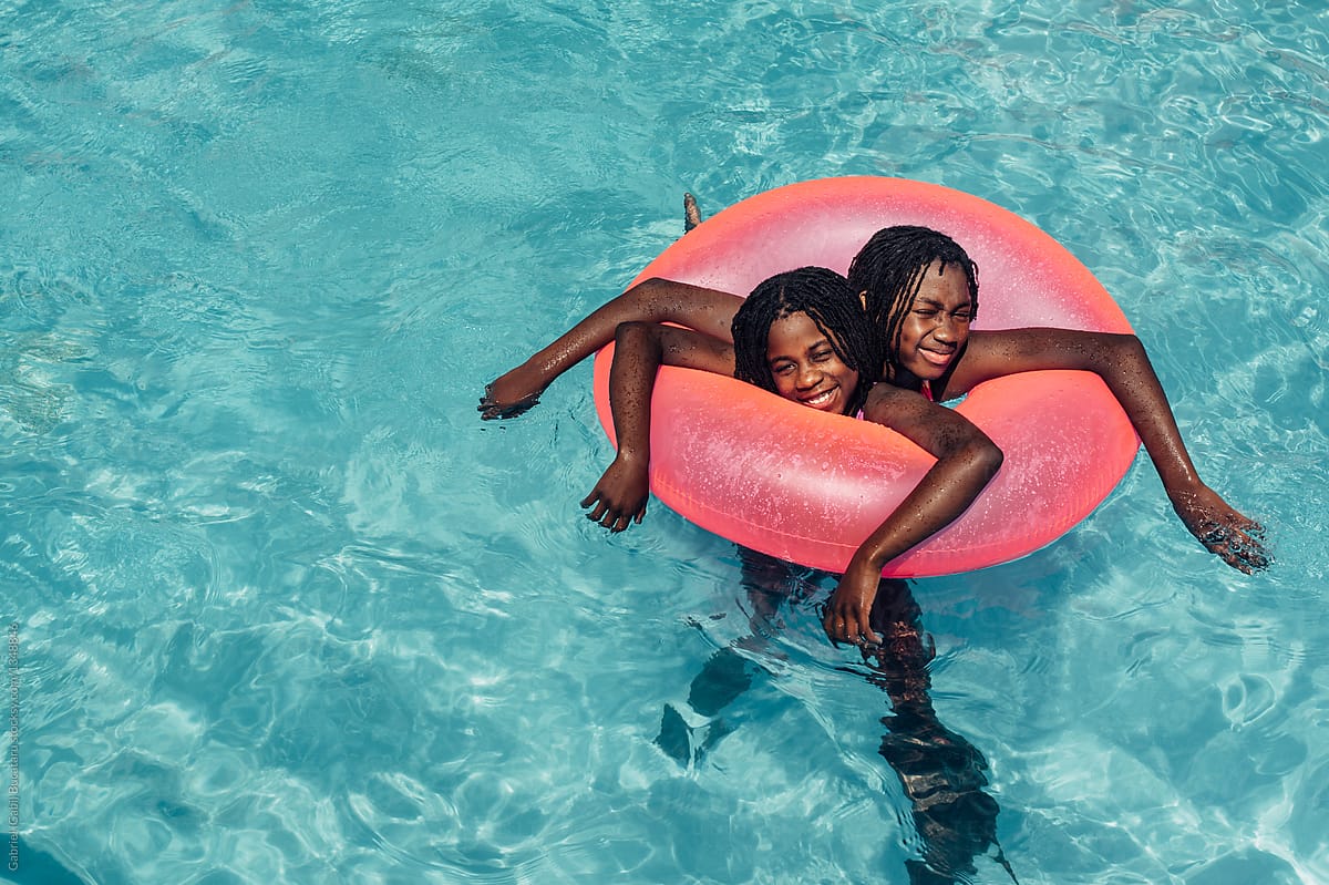 Two African American girls in a pool with a pink tube