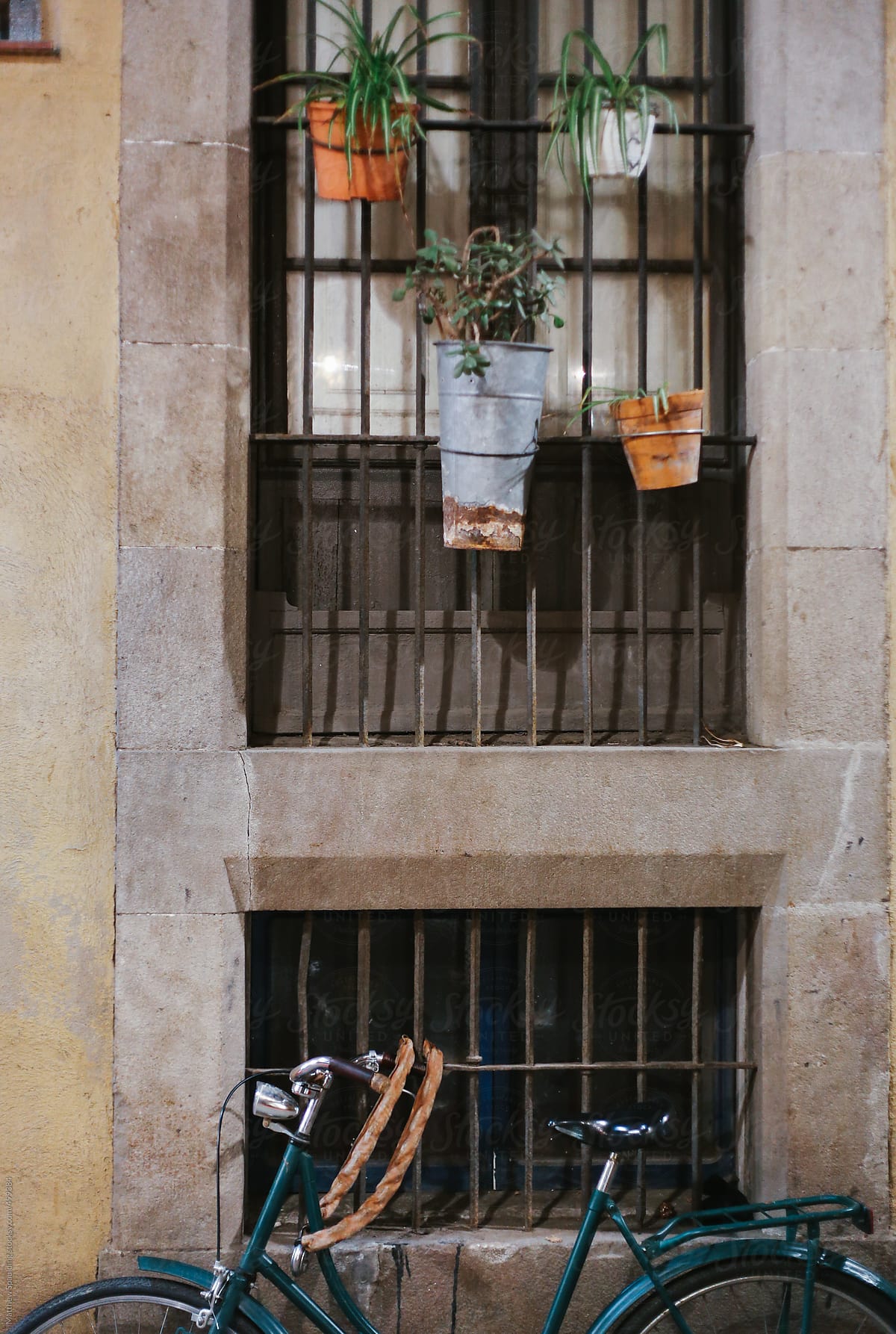Bike on sidewalk with flower pots hanging on window