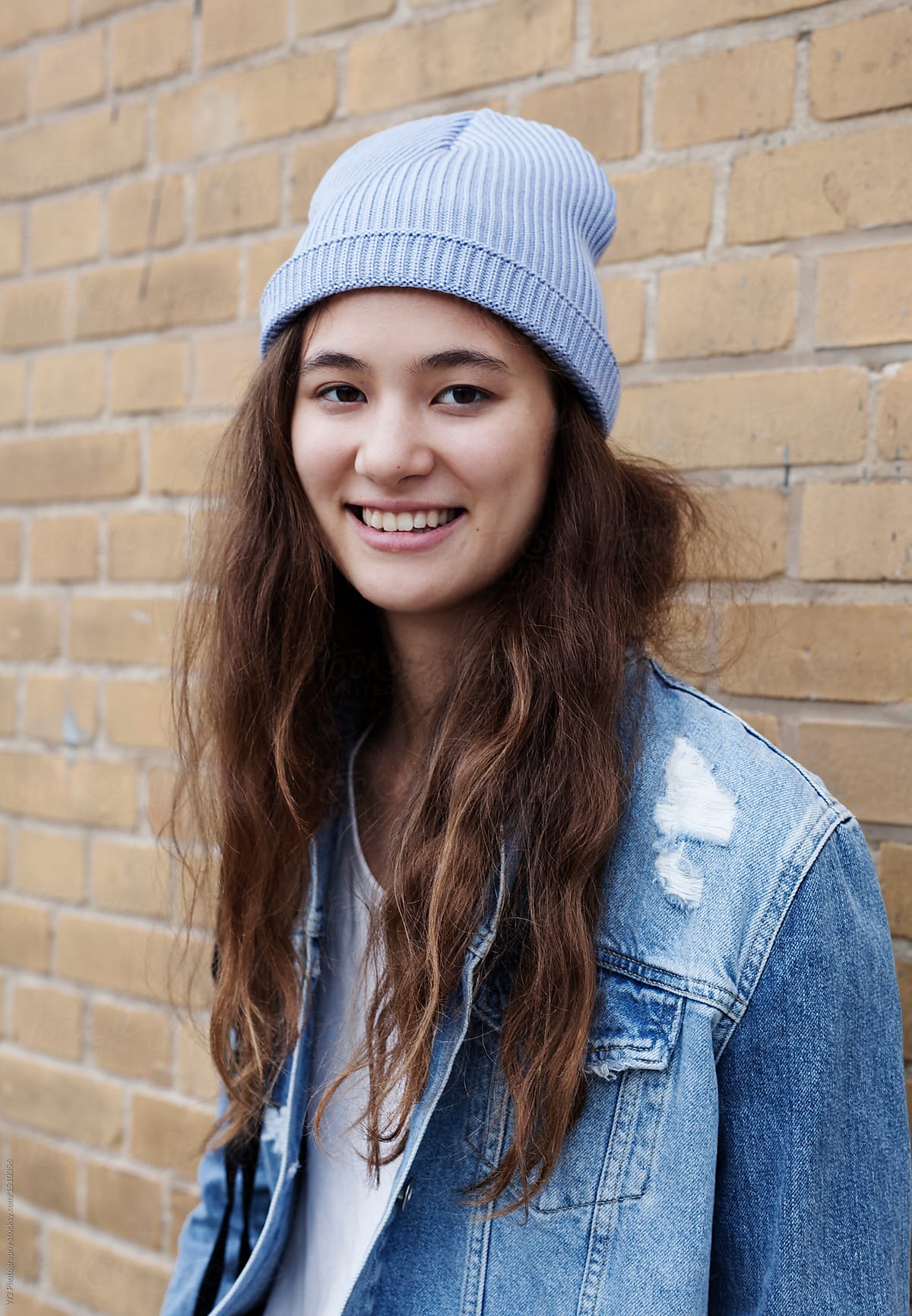 A smiling young woman against a brick wall.