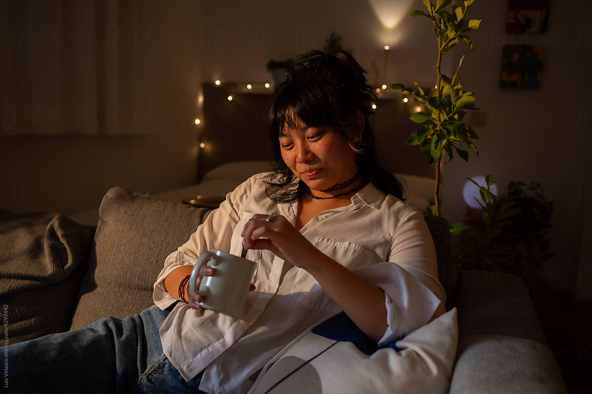 Asian Woman On The Couch At Home Having A Hot Drink.