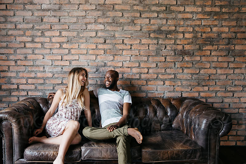 Happy multi-ethnic couple on a leather couch laughing together with big copy space